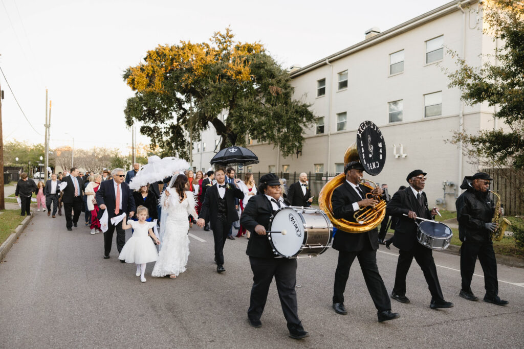 The couple leads a joyful second line parade down the street with a brass band and guests waving white handkerchiefs.