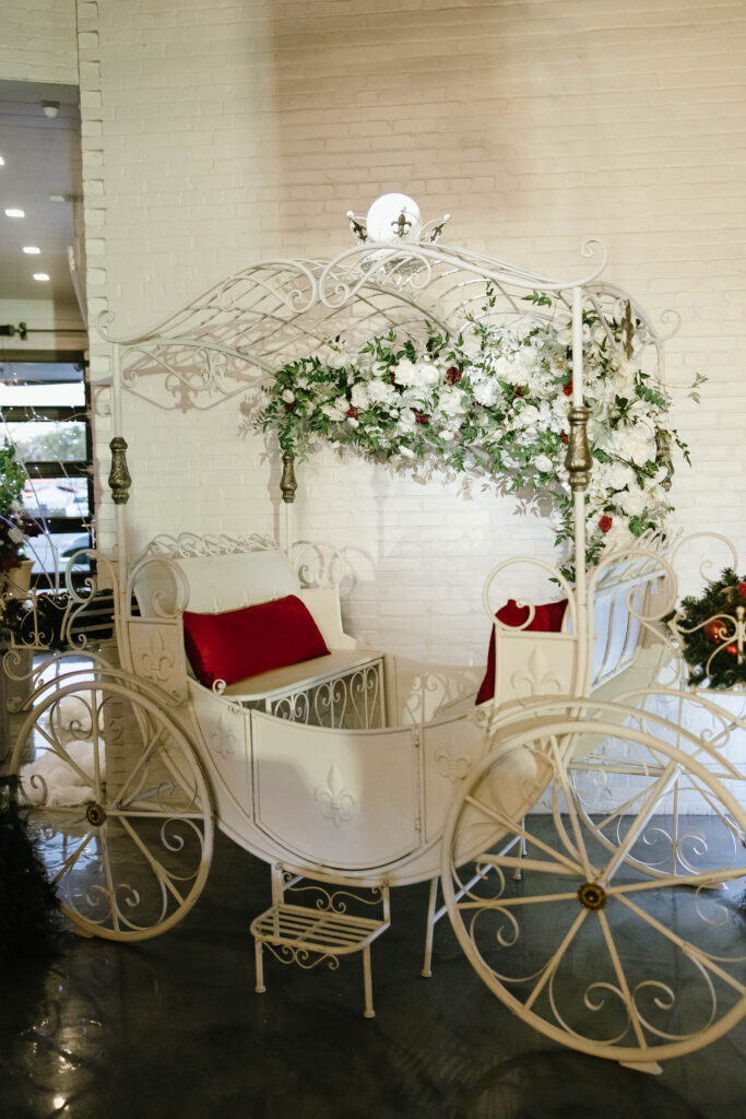 Ornate white carriage decorated with lush white and red florals displayed inside the reception venue.