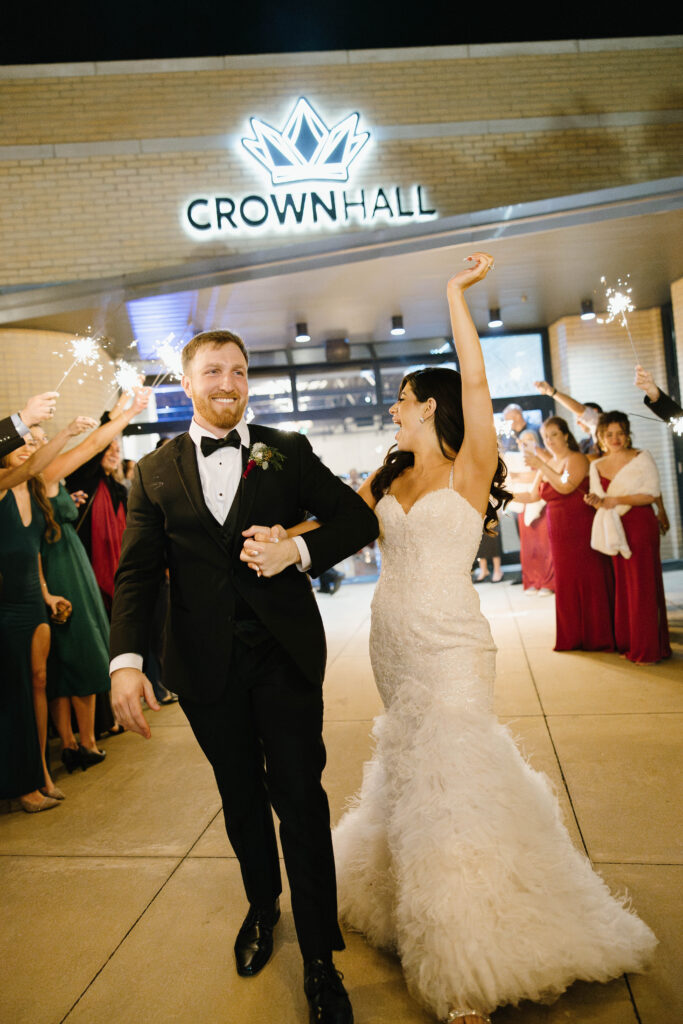 Bride and groom make their grand exit beneath sparklers outside Crown Hall, smiling as guests cheer around them.