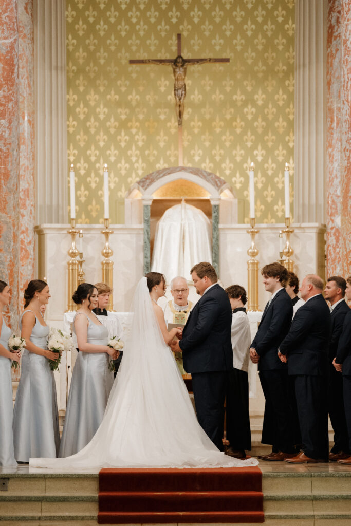 Bride and groom exchanging vows during a traditional church wedding ceremony beneath a crucifix.