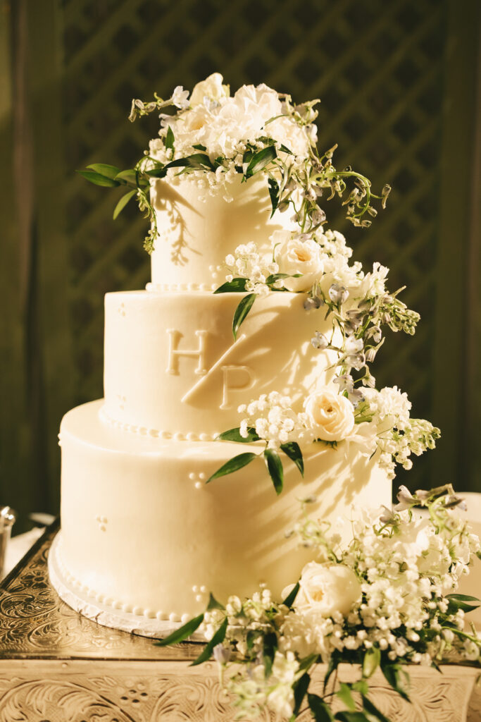 Three-tier white wedding cake decorated with cascading fresh white flowers and monogram initials