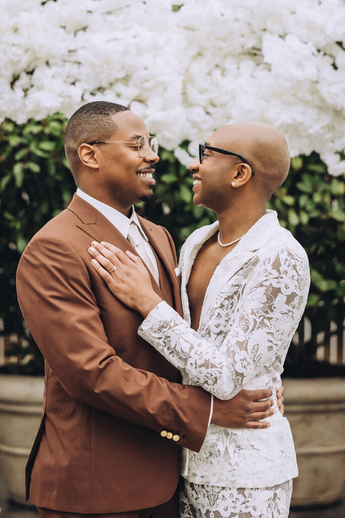 Couple embracing beneath a white floral arch during their outdoor wedding ceremony.
