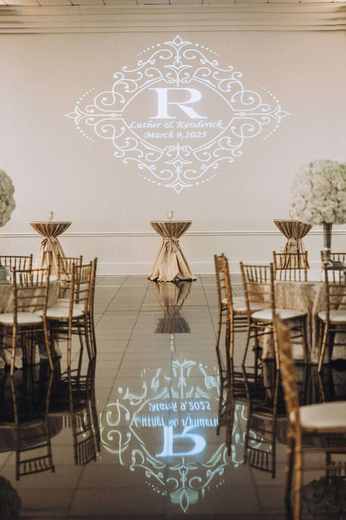 Reception ballroom with gold chiavari chairs and a monogram projection reading “Luther & Kenderick – March 9, 2025.”