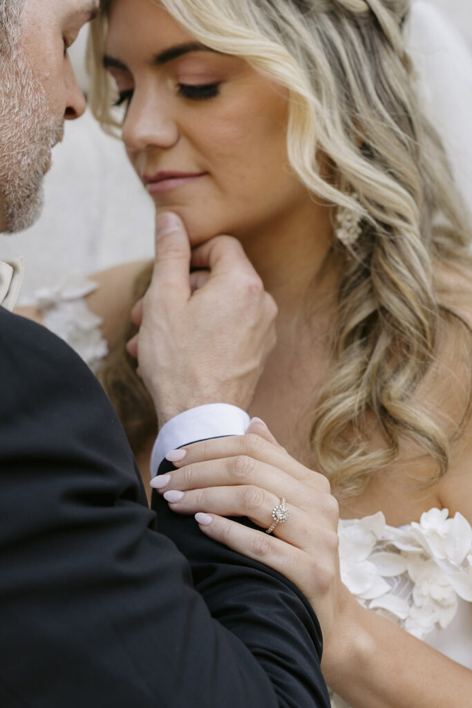 Close-up portrait of couple embracing, highlighting an engagement ring and wedding attire details.