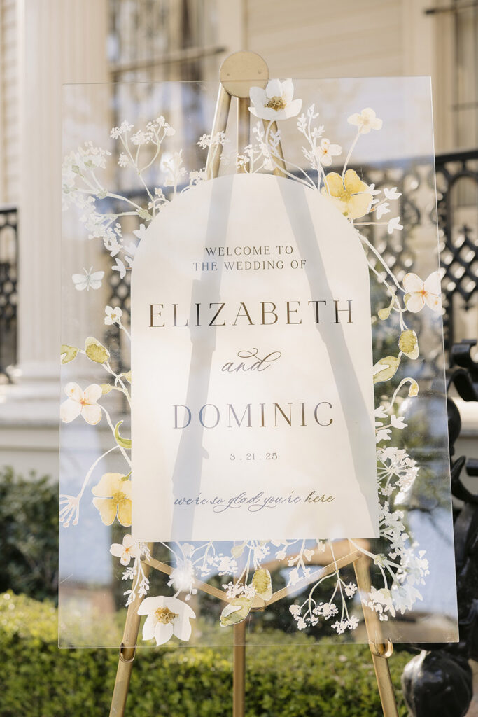 Acrylic wedding welcome sign with floral illustration reading “Welcome to the wedding of Elizabeth and Dominic.”