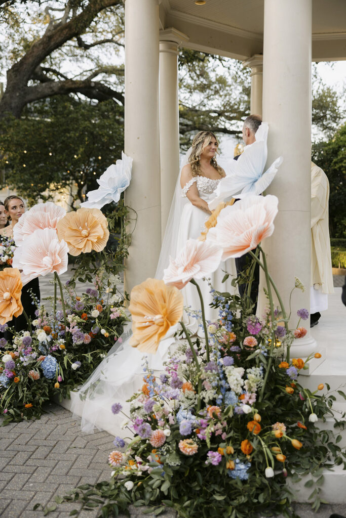 Wide view of outdoor gazebo ceremony with couple at the altar surrounded by wedding party and guests.