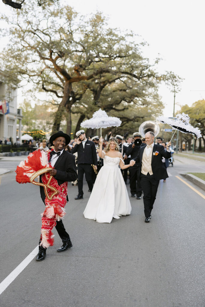 New Orleans second line wedding parade with couple walking behind a brass band and parade leader carrying a decorated umbrella.