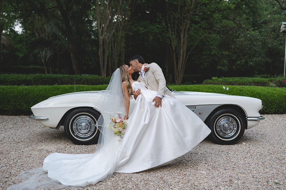 Newlyweds kissing beside a classic white vintage car during outdoor wedding portraits.