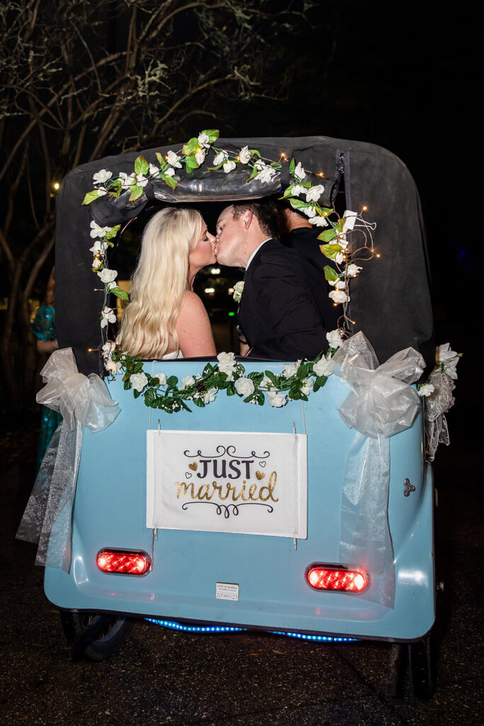 Couple kissing in a decorated getaway cart with “Just Married” sign during nighttime wedding exit.