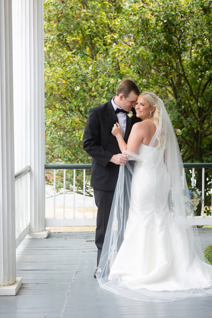 Couple embracing on a porch with greenery backdrop during wedding portraits.