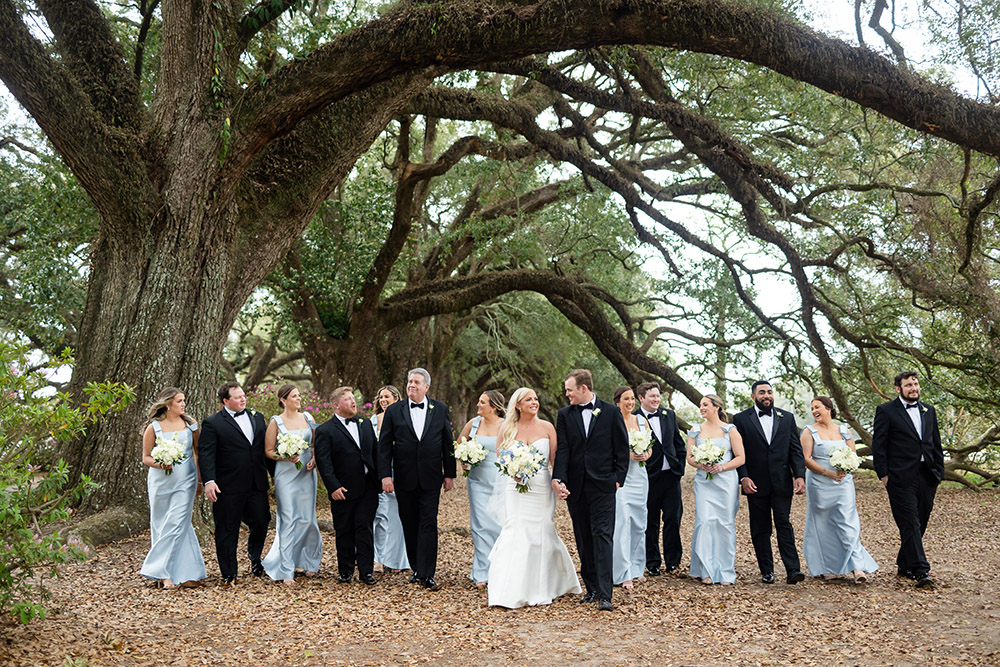Wedding party walking beneath large oak trees with hanging moss during outdoor group portraits.