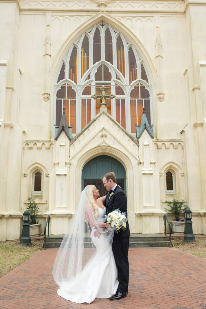 Couple embracing in front of a historic church with gothic architecture during wedding portraits.