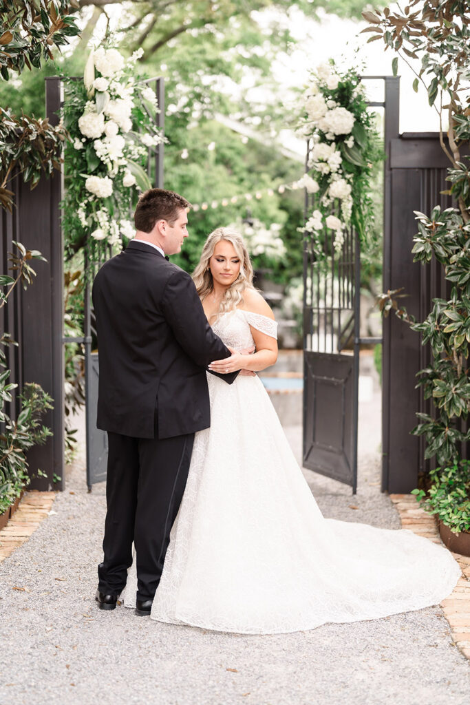 Couple posing together beneath floral-covered garden gates during outdoor wedding portraits.