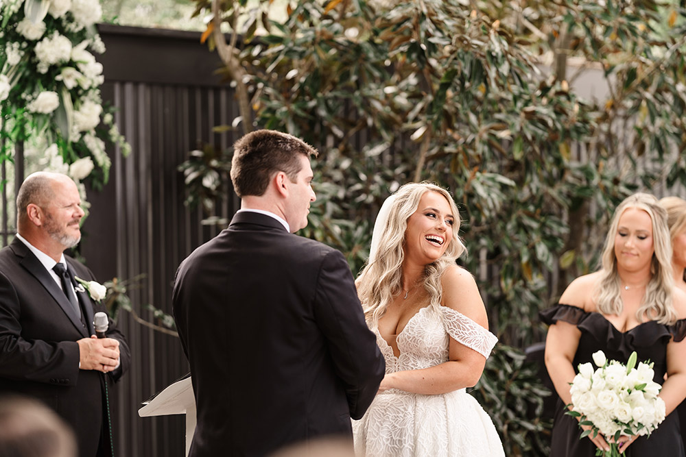 Couple exchanging vows and smiling during an outdoor garden wedding ceremony surrounded by greenery.