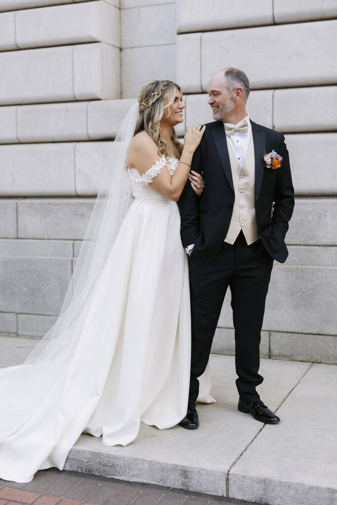 Couple standing together against a stone building wall during wedding portraits.