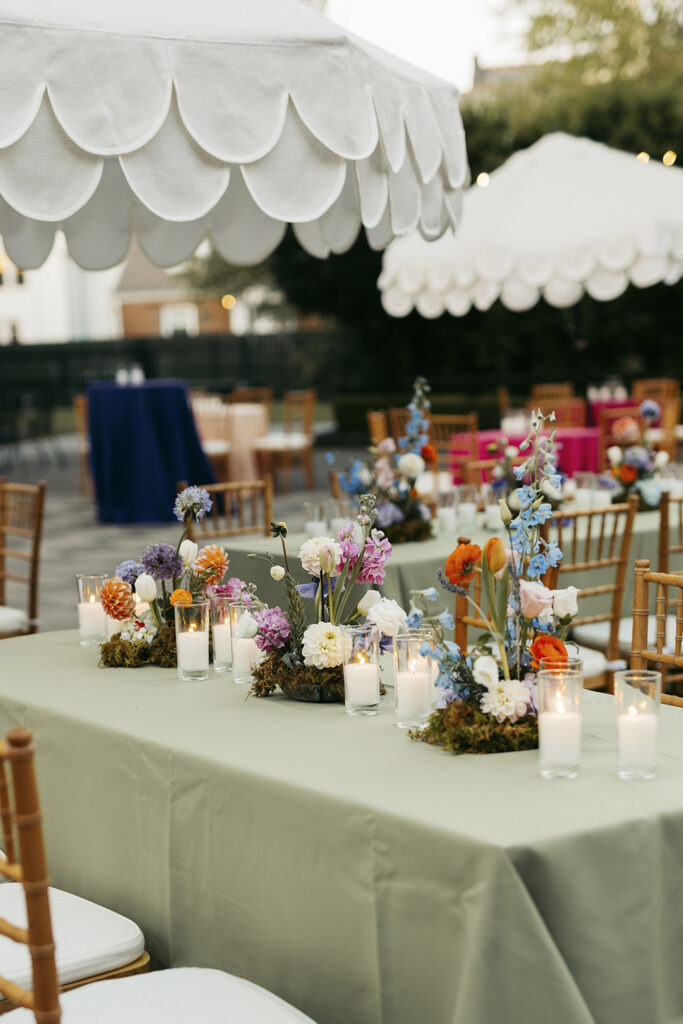 Outdoor wedding reception table with colorful garden-style flowers and candles beneath white scalloped umbrellas.