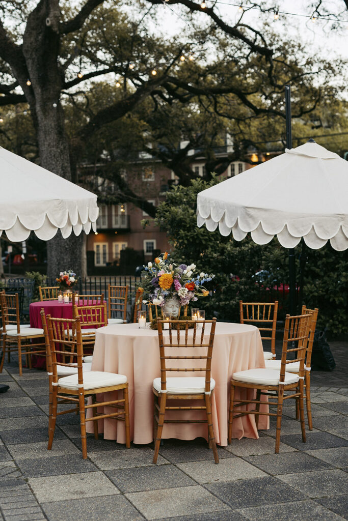 Courtyard reception tables with pastel linens, gold chiavari chairs, and floral centerpieces under string lights.