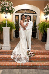 Couple posing on brick steps outside elegant wedding venue in Mobile, Alabama with tall floral arrangements