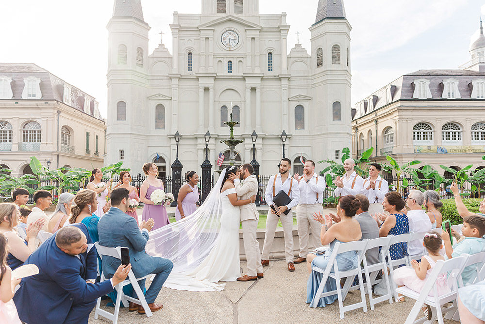 Bride and groom sharing their first kiss at Jackson Square wedding ceremony in New Orleans with St. Louis Cathedral in background