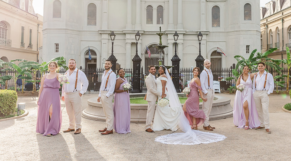 Wedding party portrait in Jackson Square in New Orleans with bride, groom, bridesmaids in lavender dresses, and groomsmen in tan suits