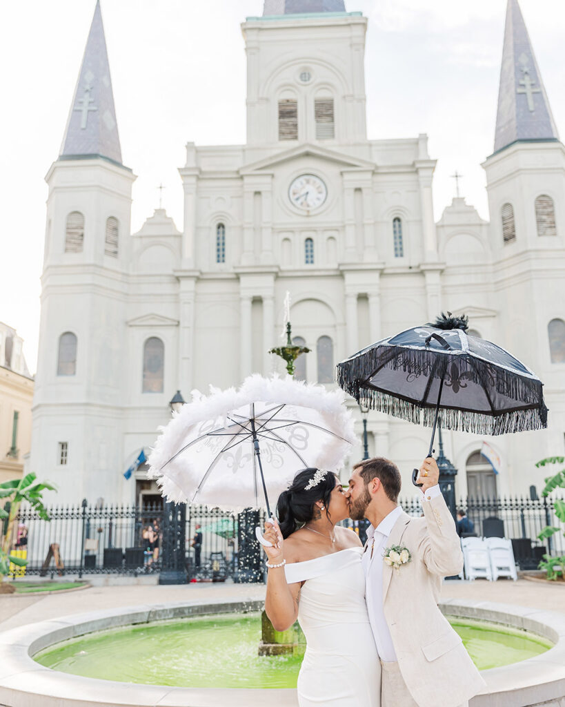 Bride and groom kissing in front of St. Louis Cathedral holding decorative second line umbrellas in New Orleans
