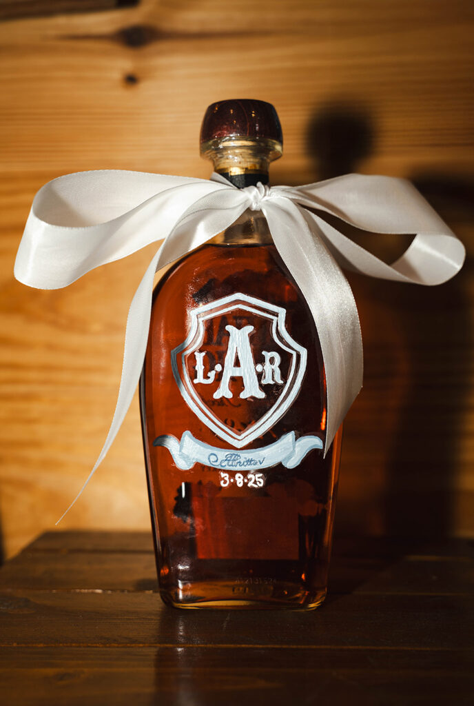 Amber glass decanter with a white ribbon tied around the neck, placed on a wooden surface.