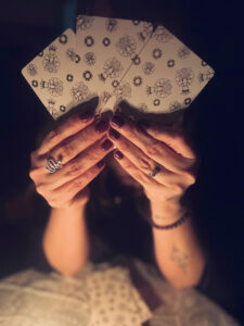 Mystic Myndee holds tarot cards fanned in her hands.