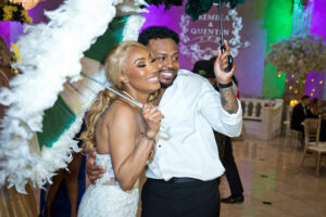 Bride and groom smiling under second line umbrellas on dance floor with colorful lighting during lively wedding reception