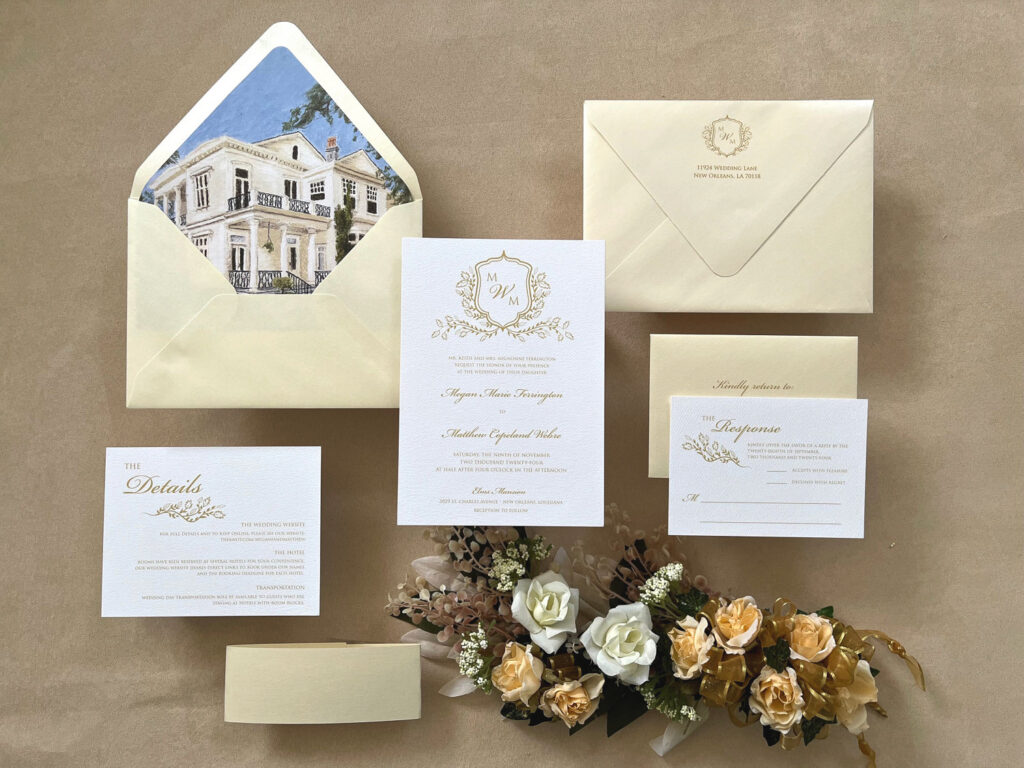 Classic ivory and gold wedding invitation suite with venue illustration envelope liner, crest monogram, RSVP card, and romantic floral styling.