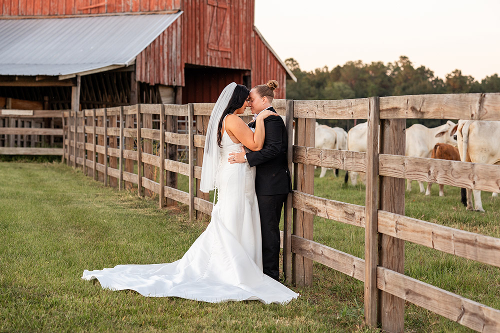 Newlywed brides making a joyful sparkler exit through cheering wedding guests inside a rustic barn venue at the end of the reception.