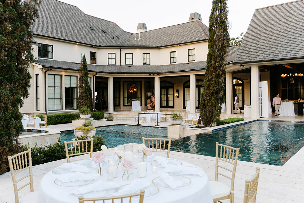 Reception tables surround a long pool courtyard at an elegant estate wedding venue during cocktail hour.