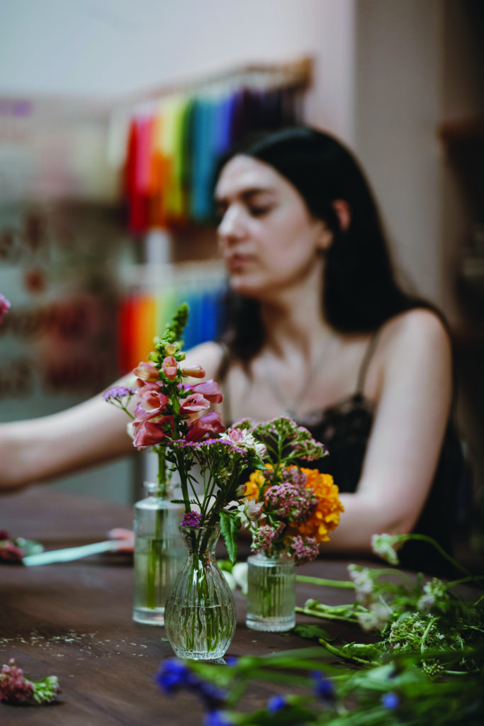 Woman arranging colorful fresh-cut flowers in small glass vases inside a floral studio workspace.