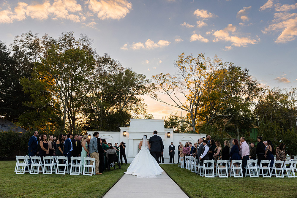 Bride and groom walking down the aisle together at sunset following their outdoor wedding ceremony as guests stand and watch.