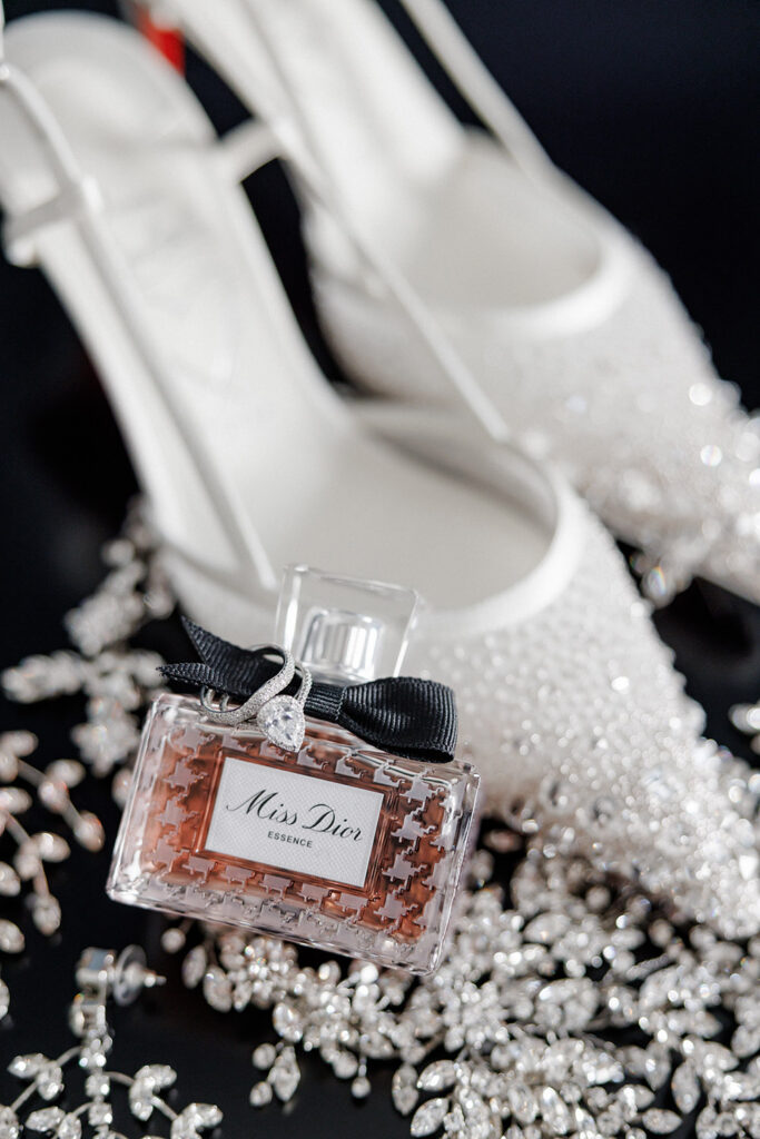 Miss Dior perfume bottle with diamond engagement ring, sparkling bridal heels, and crystal accessories styled on black fabric backdrop