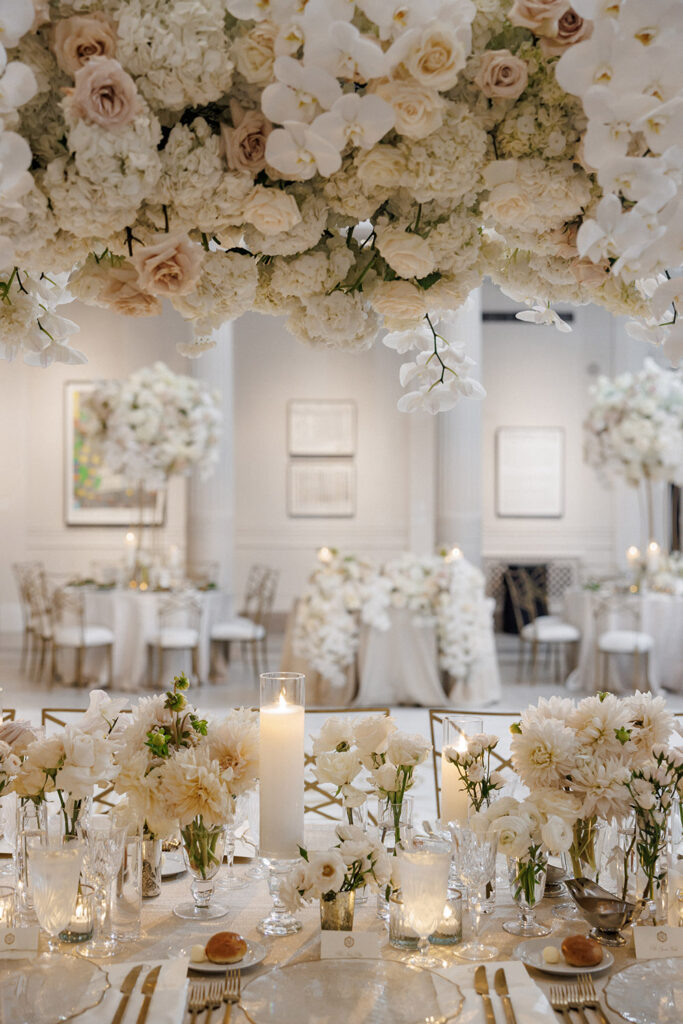 Overhead floral installation of white orchids, roses, and hydrangeas suspended above candlelit reception tables.