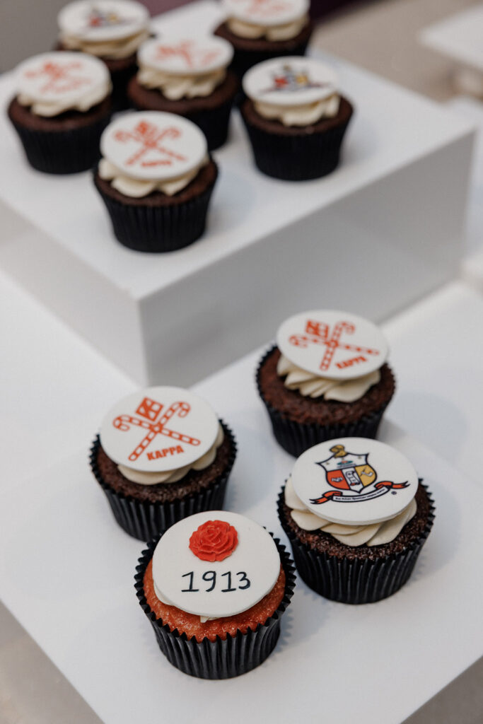 Assorted wedding cupcakes decorated with sorority and fraternity-inspired emblems and a “1913” topper.