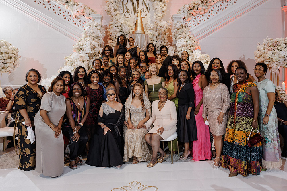 Large multigenerational group portrait gathered around the bride on the reception dance floor inside the museum venue.