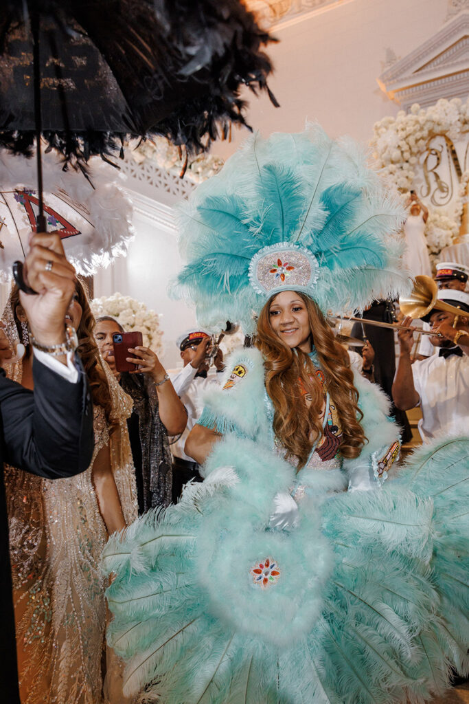 Guest in a turquoise feathered Mardi Gras Indian-inspired costume dances through the reception while musicians perform behind her.
