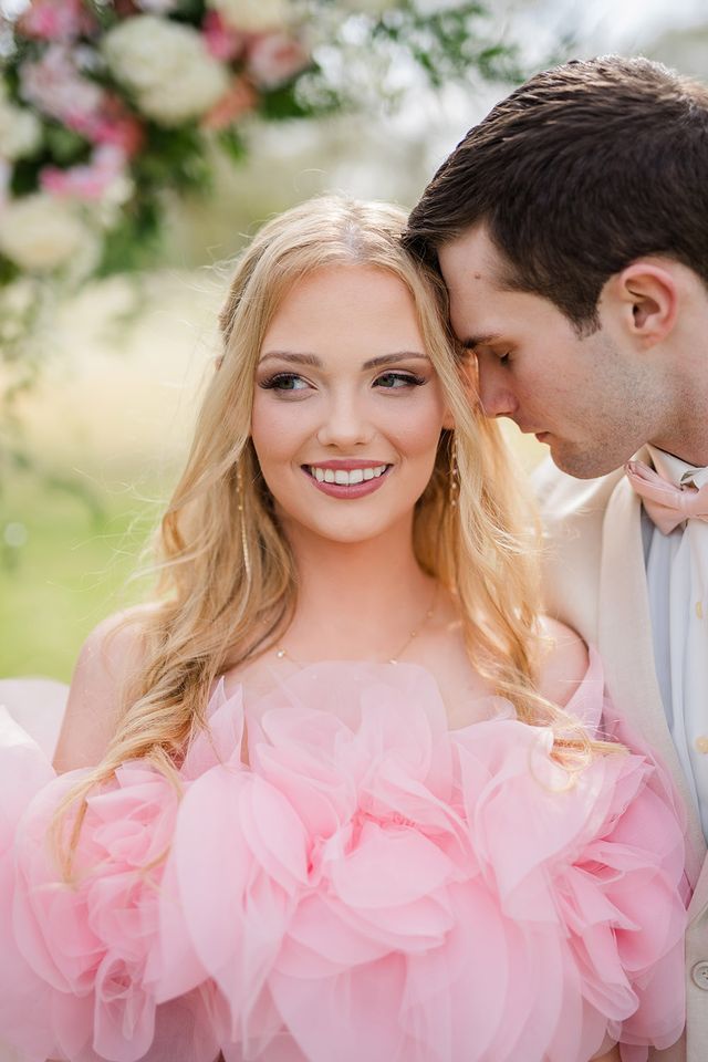 Intimate close-up of couple, bride smiling in pink ruffled gown while groom leans in affectionately