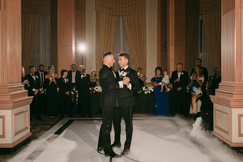 The couple shares their first dance surrounded by low-lying fog and guests gathered around the ballroom dance floor at their black-tie reception.