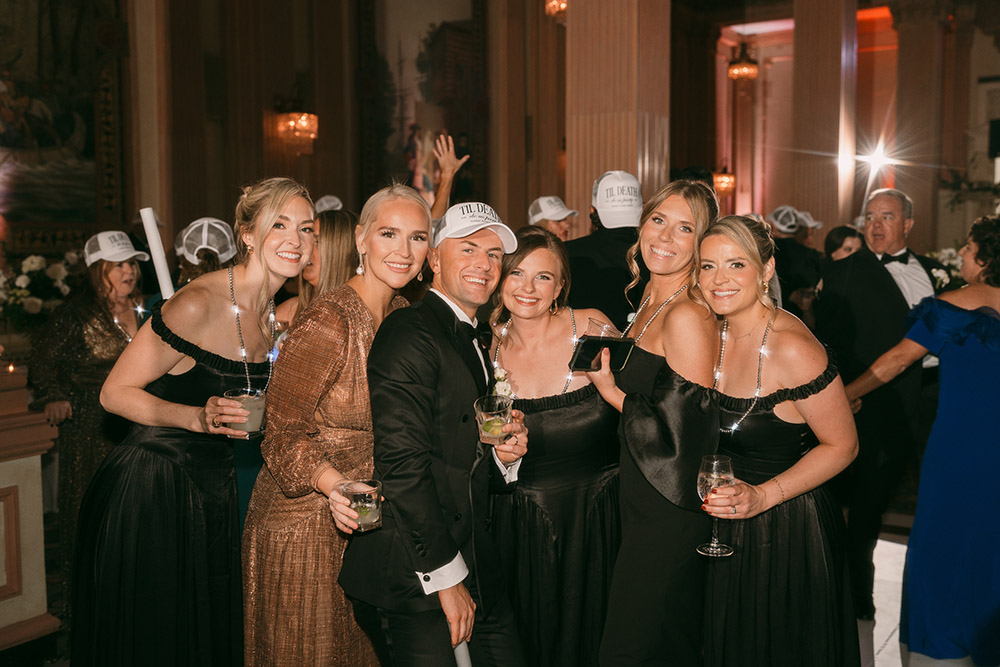 Ryan poses with friends on the dance floor while guests celebrate in custom “’Til Death Do Us Party” hats during the reception.
