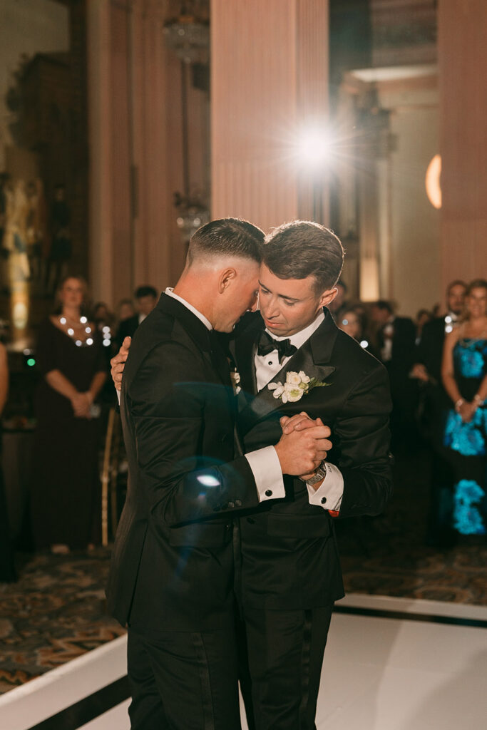 The couple shares an emotional first dance beneath dramatic spotlighting during their elegant ballroom reception.