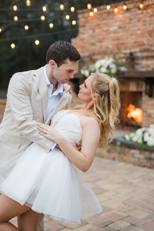 Romantic dip pose of bride and groom in front of brick fireplace with glowing string lights