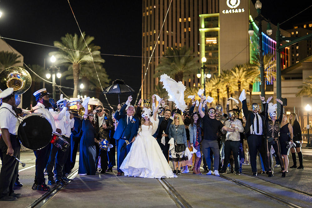 Newlyweds celebrate in the middle of a New Orleans street with guests, masquerade masks, and a brass band during a festive second line wedding parade.