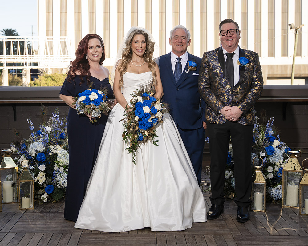 Newlyweds pose with family members during rooftop wedding portraits surrounded by blue and white floral ceremony arrangements and lantern accents.