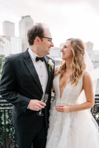 Newly married couple sharing champagne and smiling at one another on a wrought-iron balcony in downtown New Orleans at sunset.