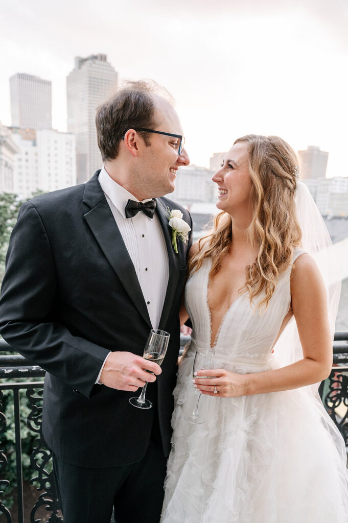Newly married couple sharing champagne and smiling at one another on a wrought-iron balcony in downtown New Orleans at sunset.