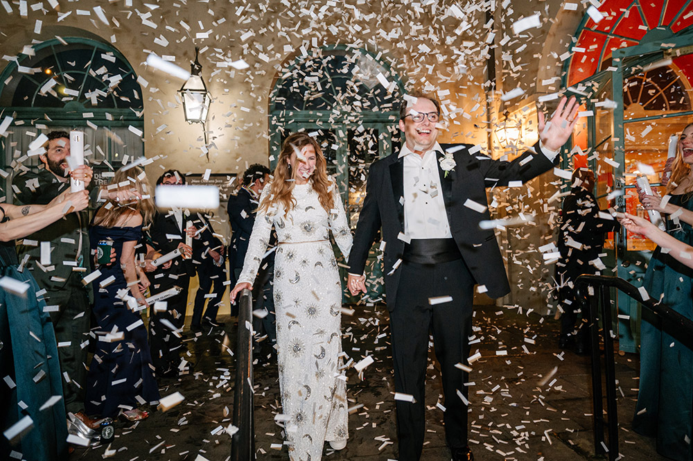Newlyweds making a festive confetti-filled grand exit in New Orleans while guests cheer and celebrate around them.