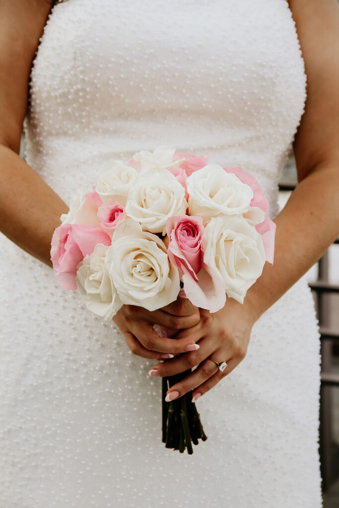 Close-up of the bride holding a bouquet of white and pink roses against her beaded wedding gown.