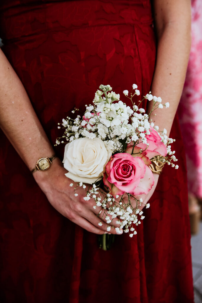 Bridesmaid holding a bouquet of white and pink roses with baby's breath against a burgundy dress.